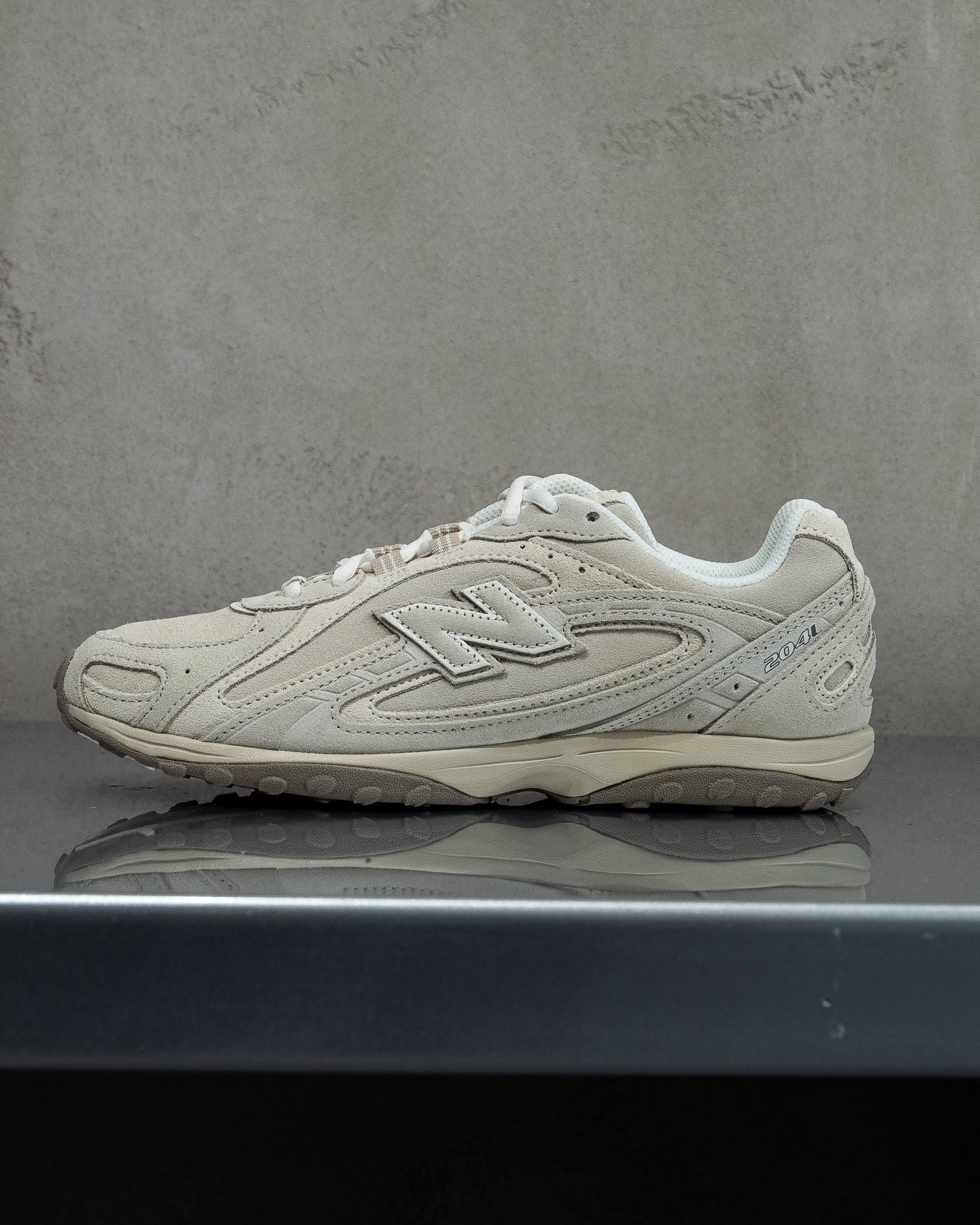 White New Balance sneaker on a reflective surface with a gray background